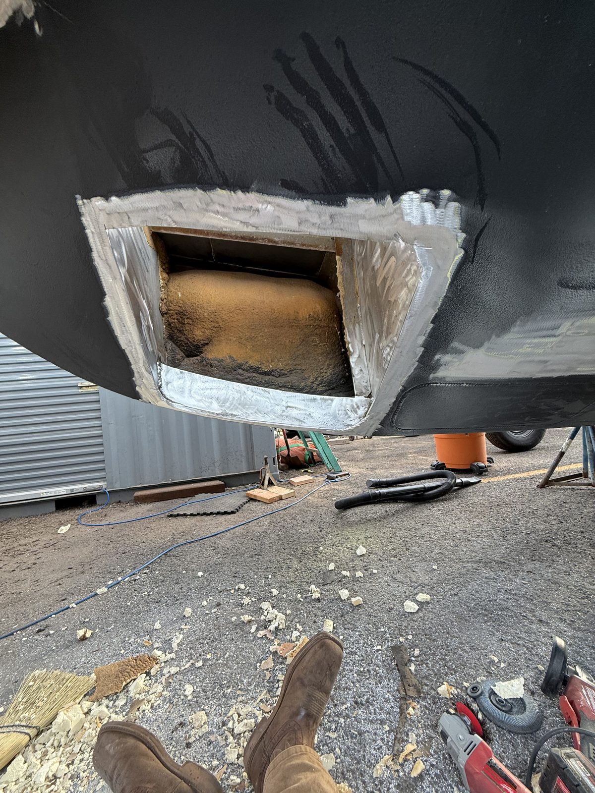 Corroded section cut out of a black aluminum hull, edges ground bright and ready for new plate